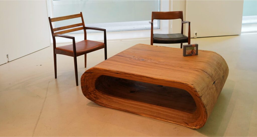 OZE handcrafted wooden coffee table displayed with vintage chairs in gallery space