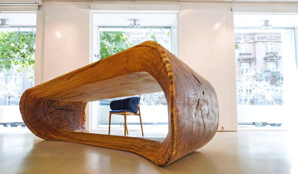 Low-angle view of OZE sculptural wooden table’s open-core form in a bright gallery